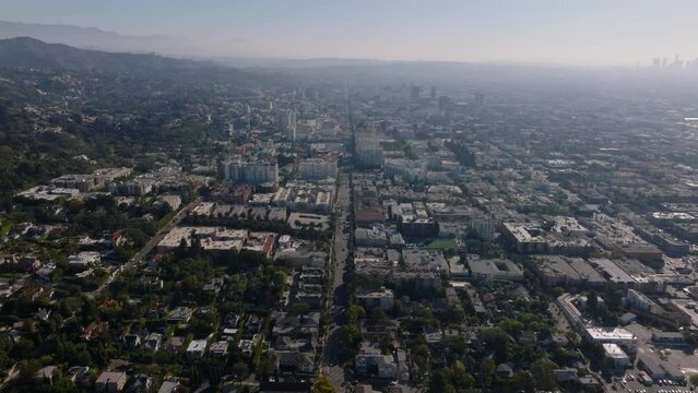 Aerial panoramic view of buildings in metropolis. Backwards reveal houses in residential urban district. Hazy view against sunshine. Los Angeles, California, USA