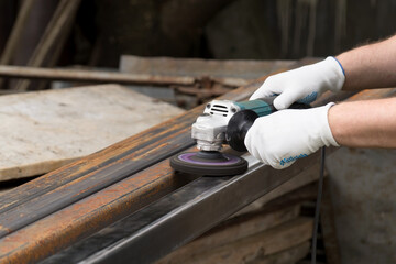 A man working with electric angle grinder tool. Removing rust a metal square tube. Hands in white...