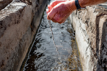 Blurred Caucasian elderly man's hands collect fresh water from a stream to quench their thirst during a walk. Focus on the drops