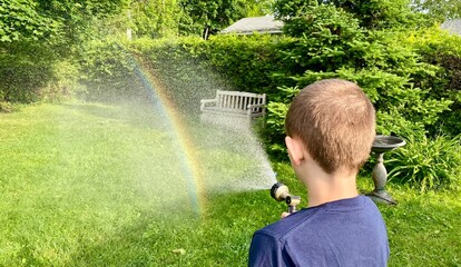 Happy child outdoors making  water rainbows with the hose in the lovely morning sunlight.