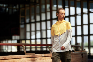 Fototapeta premium Young sportswoman girl is warming up before training at the stadium. A slender blonde in a yellow-gray sports jacket is concentrating before the competition. sports and recreation. Half length photo.