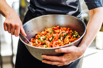 frischer, gesunder Tomatensalat in einer großen Schüssel. Hand hält die Schüssel, Hand rührt den Salat. Tomaten, Petersilie, Feta, Lauchzwiebeln, Frühlingszwiebeln