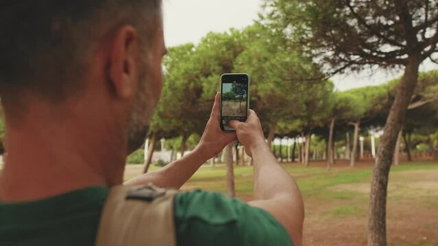 Close up, middle-aged man takes photo on smartphone while standing in city park