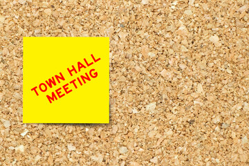 Yellow note paper with word town hall meeting on cork board background with copy space