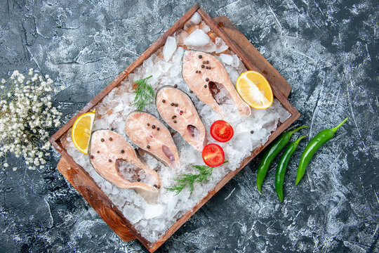 top view raw fish slices with ice on wood board green hot peppers on table