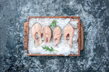 top view raw fish slices with ice on wood serving board on grey background