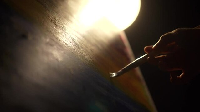 Close-up Moving Paint brush holding on hand of artist and painting on canvas work art with color oil painting at dark room workshop. Artist works and Creative on Abstract Oil Painting at night.