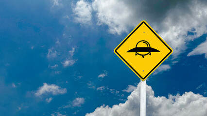 Yellow sign with painting of the UFO with clouds and blue sky in background concept of UFO...