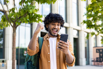 Young hispanic student celebrating victory and happy good news online, man reading page interent...