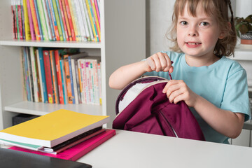 Girl fastens her backpack, from which she took out books and stationery. Preparation for school....