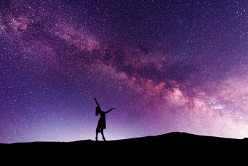 Woman silhouette dancing in the night, on the bright Milky Way Galaxy background.