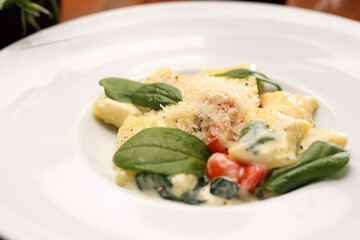 Ravioli pasta in cream sauce with basil and tomatoes, on a white plate, close-up.