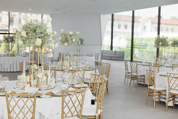Served wedding tables with golden plates, decorative fresh  white roses and gypsophila flowers and...