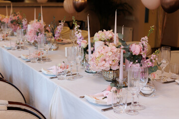 Wedding decorations. Served wedding table with decorative fresh pink flowers and candles. Celebration details. Flower composition roses plates and candles in candlesticks