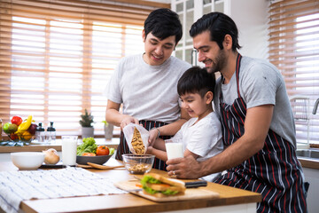A couple of gays and adopted son family preparing meal together with fun happiness and laughing in kitchen at home, Boy pouring cerial in a glass bolw.