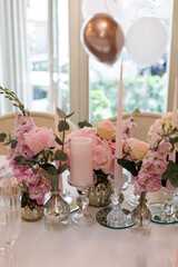 Close up decorative composition of greenery, fresh white and  pink flowers, white candles on a festive table with a white tablecloth. Concept of wedding decorations 