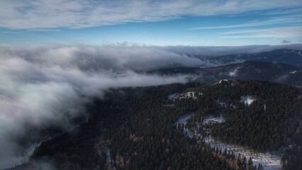 View from above over forest area in winter with clouds passing by, drone shot (when the fog clears)