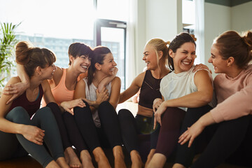 Smiling female friends sitting on gym floor after yoga class