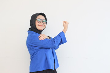 beautiful young Asian Muslim woman, wearing glasses and blue blazer with strong gesture by lifting her arms and muscles