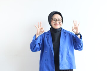beautiful young Asian Muslim woman, wearing glasses and blue blazer with hand gesture of approval or OK