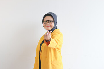Beautiful young Asian Muslim woman, wearing glasses and yellow blazer gesturing korean love sign while smiling