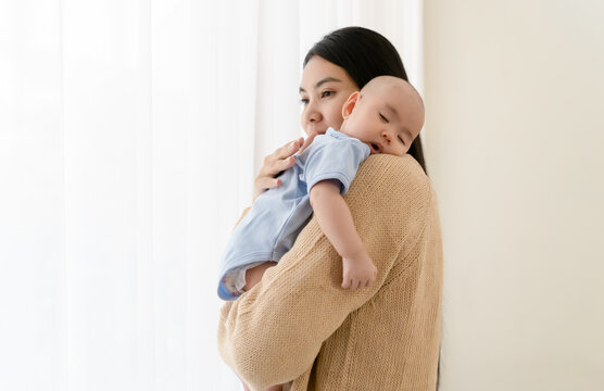 Loving Asia mom carying of her newborn baby at home. Caring young Asian mother hold lean to chest cute little infant toddler, relax enjoy tender family moment. Beautiful family, Childcare concept