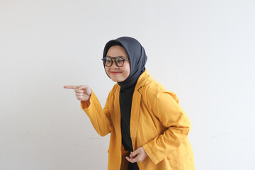 Beautiful young Asian Muslim woman in glasses, hijab and wearing yellow blazer smiling confident and happy with both hands pointing sideways