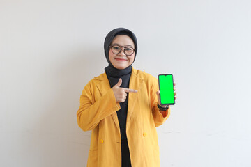 smiling beautiful asian women in yellow blazer and hijab showing green screen mobile phone