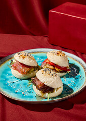 Delicious bao buns with beef, tuna, and vegetables on a blue ceramic plate on a red tablecloth. A vibrant red monochrome background highlights the colorful meal