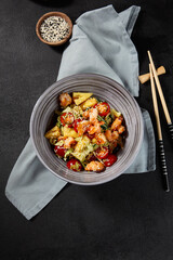 Overhead view of an Asian salad with shrimps and pineapples in a bowl on a black background, textile napkin next to the bowl