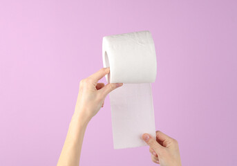Hands holding roll of white toilet paper on purple background