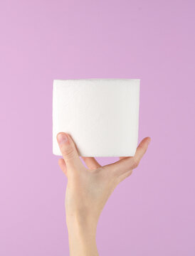 Hand Holding A Roll Of White Toilet Paper On Purple Background