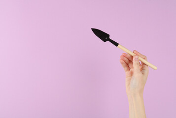 Hand holding mini gardening tool (shovel) on purple background
