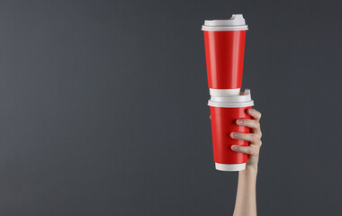 Female hand hold red disposable cups for hot drinks on a dark background