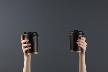 Female hands holding two disposable cups for hot drinks on a dark background