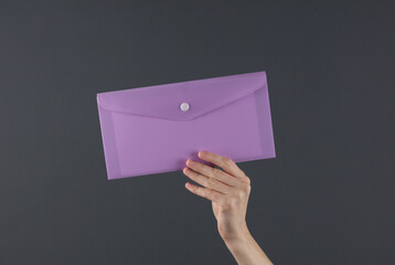 Female hand holding purple plastic envelope folder on a dark background. Business concept