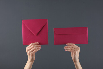 Female hands holding two pink envelopes on a dark background