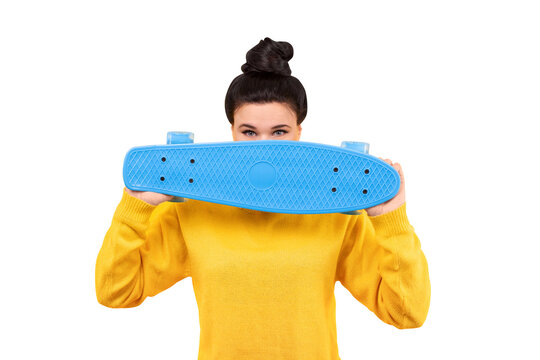 Woman in a yellow pullover with stylish classic bun, covers face with a blue skateboard, isolated on transparent background