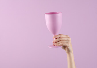 Hand holding a plastic glass goblet on a lavender color pastel background