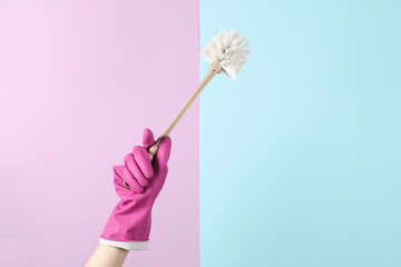 Hand in a rubber glove holds toilet brush on pastel background