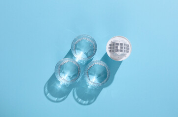 Cartridge filter for filtering water and glasses of clean water on blue background with shadow. Health Care.