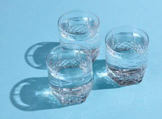 Glasses of water with reflection and shadow on blue background. Minimalism.