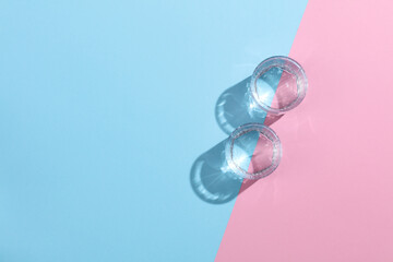 Glasses of water with reflection and shadow on pink blue pastel background. Minimalism. Top view