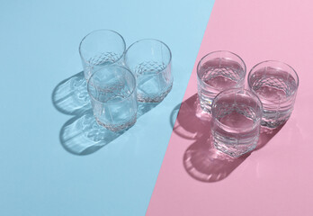 Empty and Glasses of water with reflection and shadow on pink blue pastel background. Minimalism.