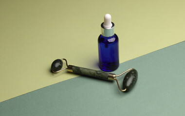 Massage jade roller and serum bottle on green background. Beauty concept