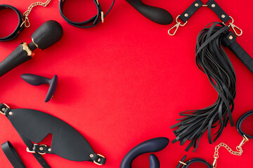 Indulge in power dynamics with erotic BDSM toys. Top view of leather whip, handcuffs, blindfold, anal plug, vibrator and dildo on red background with empty space for text or advertisement