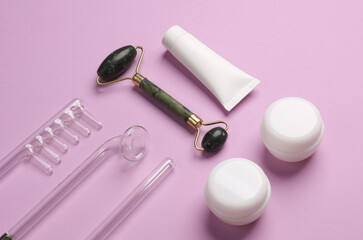 Acne treatment. Nozzles for local darsonvalization, jade roller, cream tube and jar on a purple background. Beauty concept.