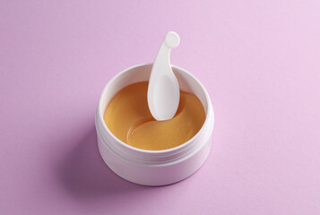 Jar with golden eye patches on purple background. Beauty concept