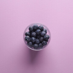 Glass of blueberries on a lavender background. Minimal food still life
