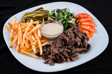 Beef goulash with French fries, tomatoes, pickled cucumbers, onion and parsley salad and sauce.